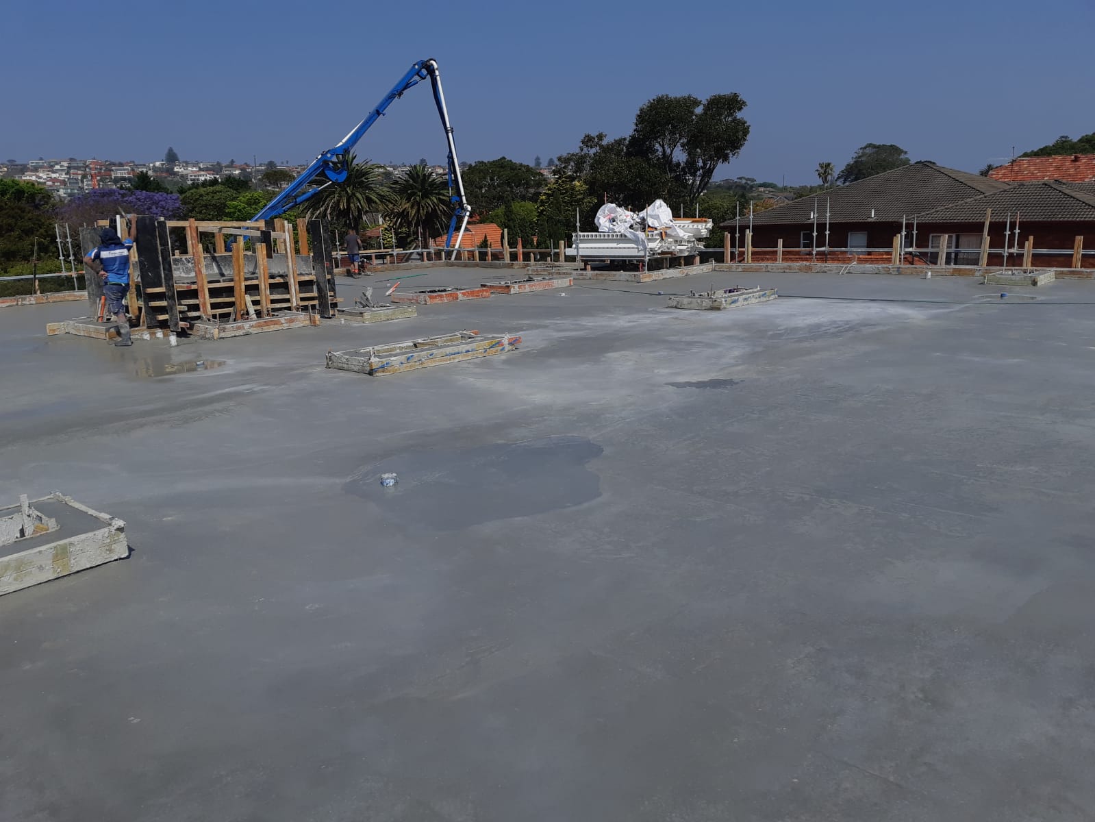 Construction site with a blue concrete pump pouring a large concrete slab outdoors.