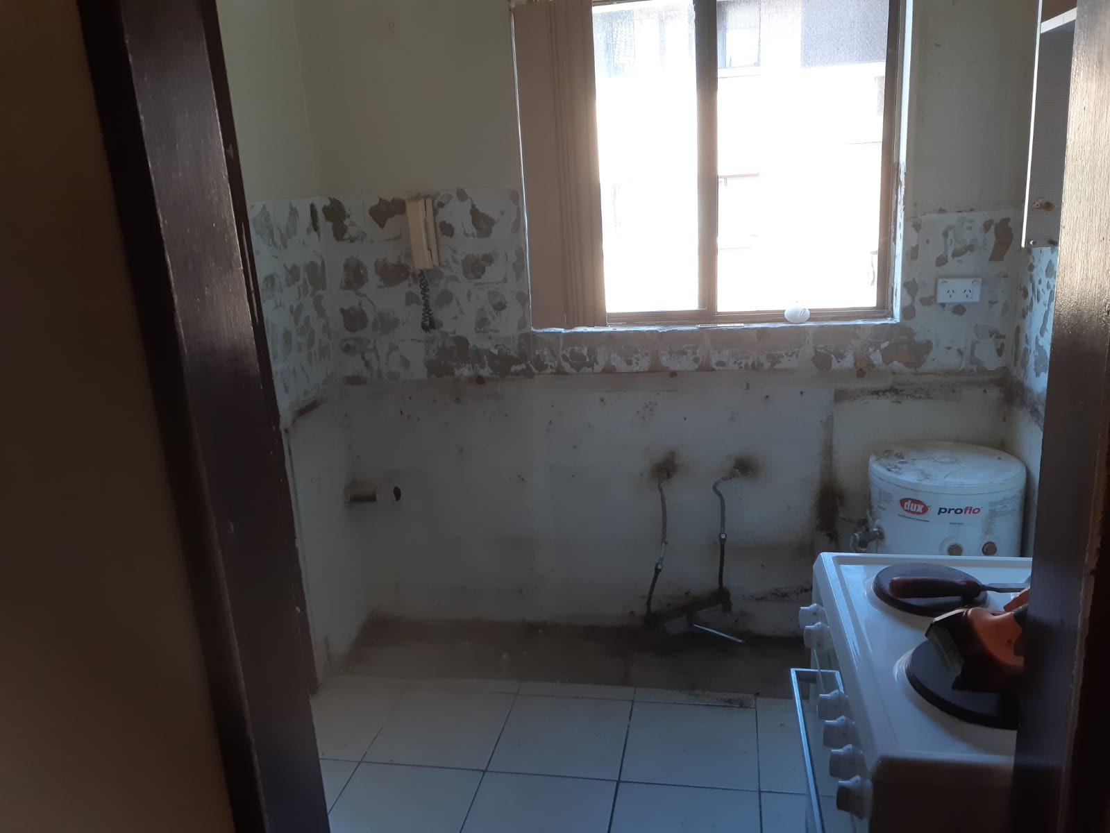 Small kitchen with peeling walls, tiled floor, window, and a stove with a pot and pan.