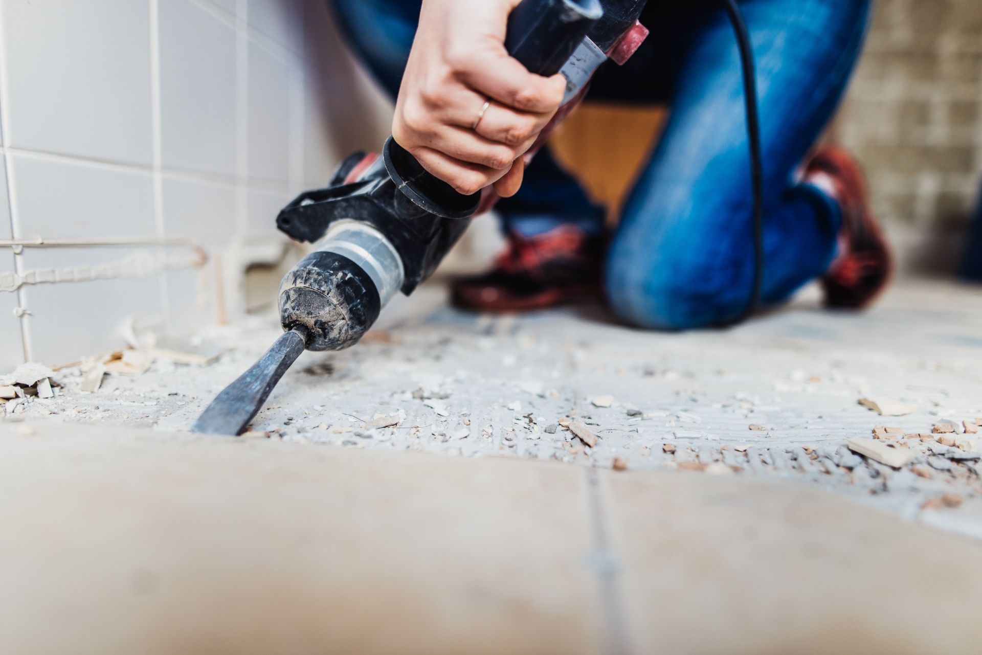 Person using a power drill to remove tile from a floor during renovation