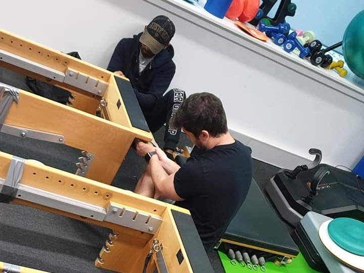 Two people working on a pool table in a game room, with tools and equipment nearby