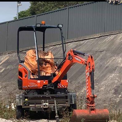 Orange mini excavator with a front roller attachment working beside a sloped concrete wall