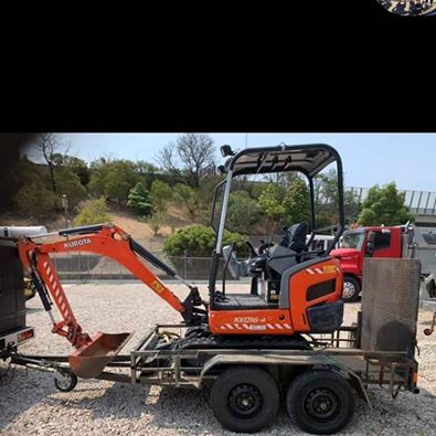 Orange mini excavator on a trailer at a construction site under a clear sky