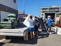 People unloading furniture from a truck into a parking lot under a clear blue sky
