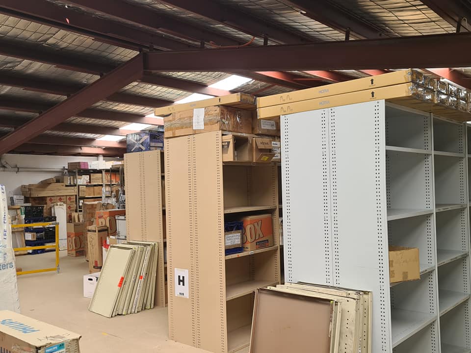 Warehouse aisle with stacked white shelving units and cardboard boxes under a metal roof