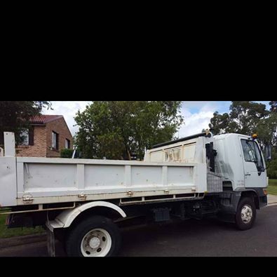 White dump truck parked on a street beside houses and trees