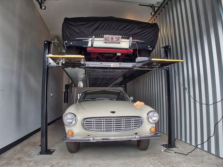Image of a luxury car storage bay containing two cars - one on a lift, the other below