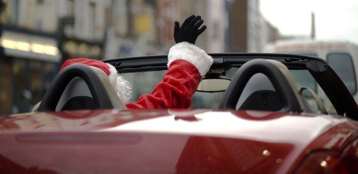 Photo of a man dressed as Santa Clause driving an exotic red car