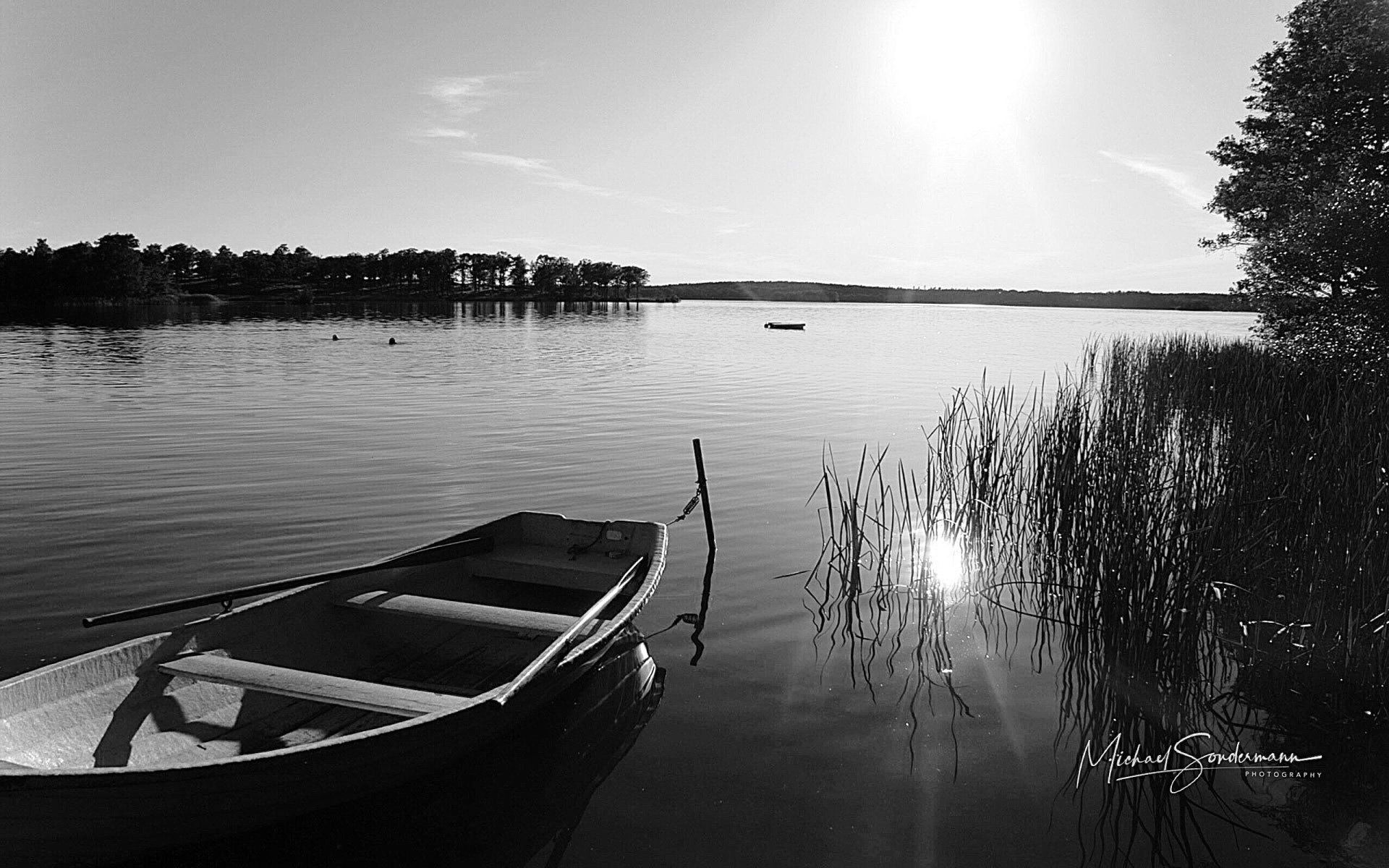 Ein schöner See mit einem Ruderboot im Vordergrund in schwarz weiss Optik.