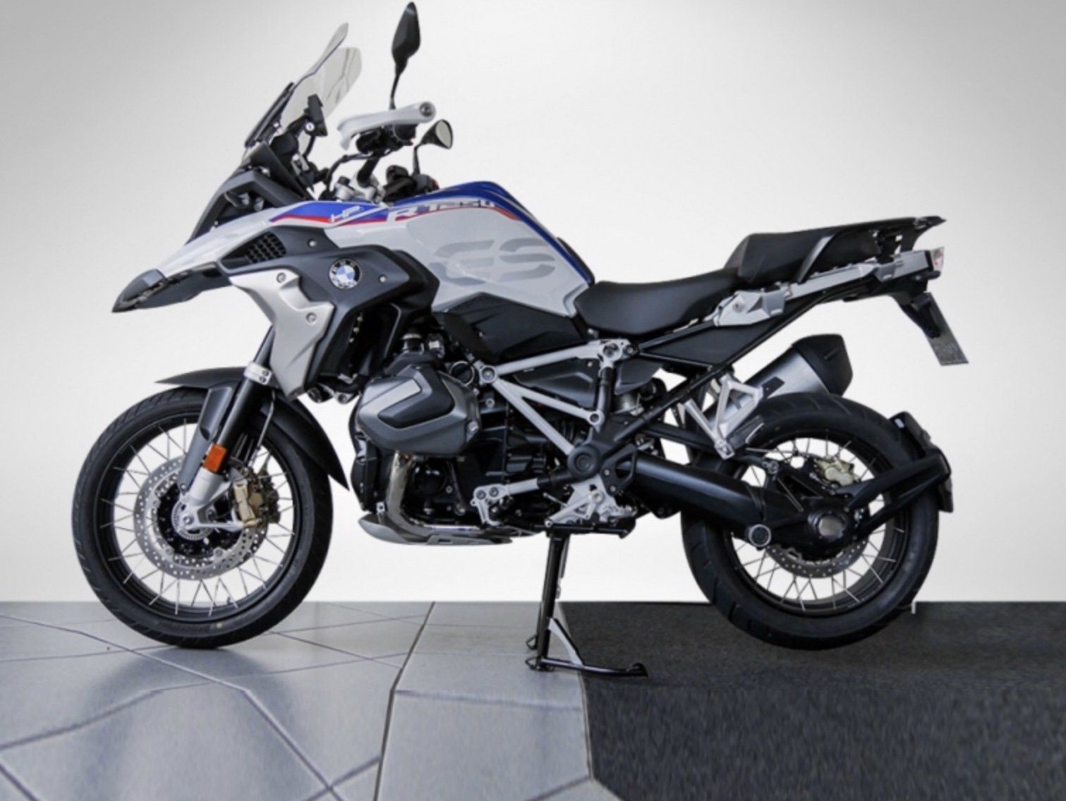 Ein Motorrad steht auf Bodenfliesen in der Seitenansicht vor einer weißen Wand auf dem Ständer