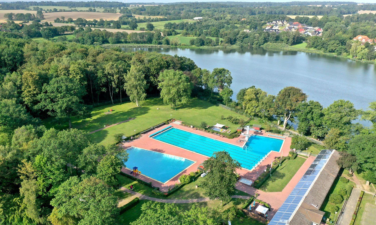 Eine Luftaufnahme eines Swimmingpools, umgeben von Bäumen und einem See
