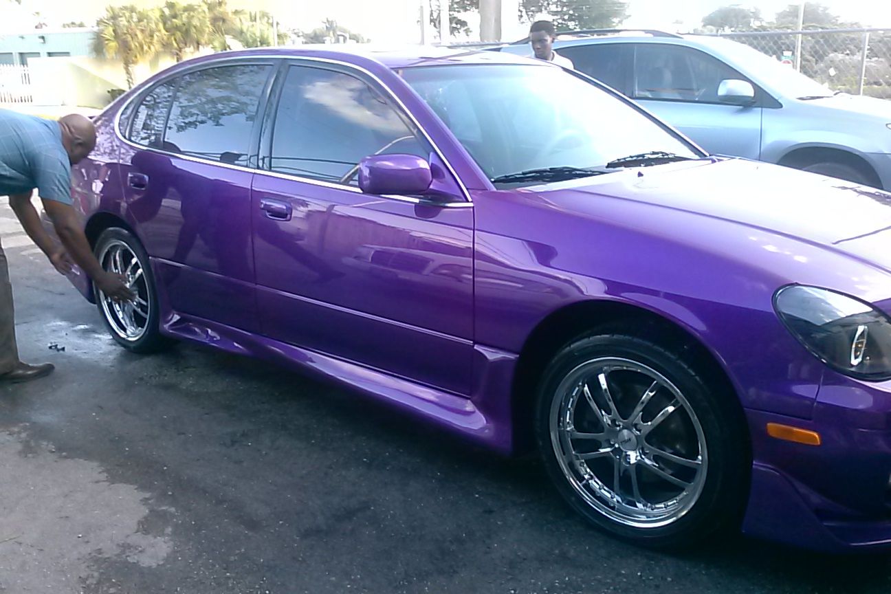 A man is washing a purple car in a parking lot