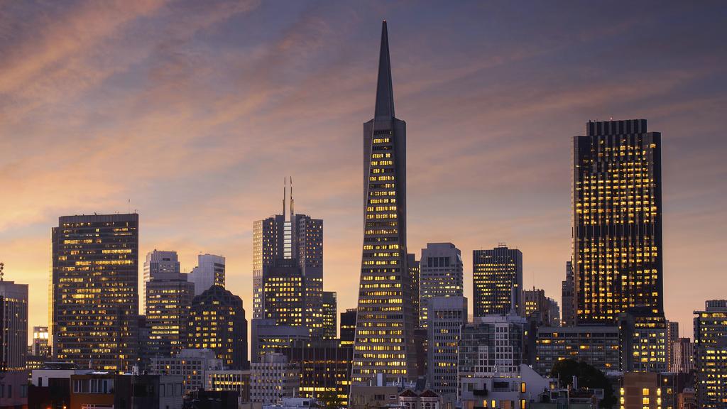 City skyline at dusk with illuminated buildings and a tall central skyscraper against a purple-orange sky