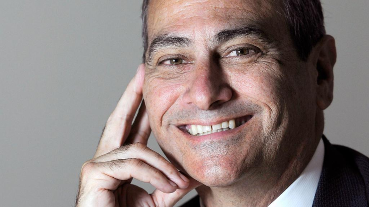 Smiling man in a suit resting his face on his hand against a gray background