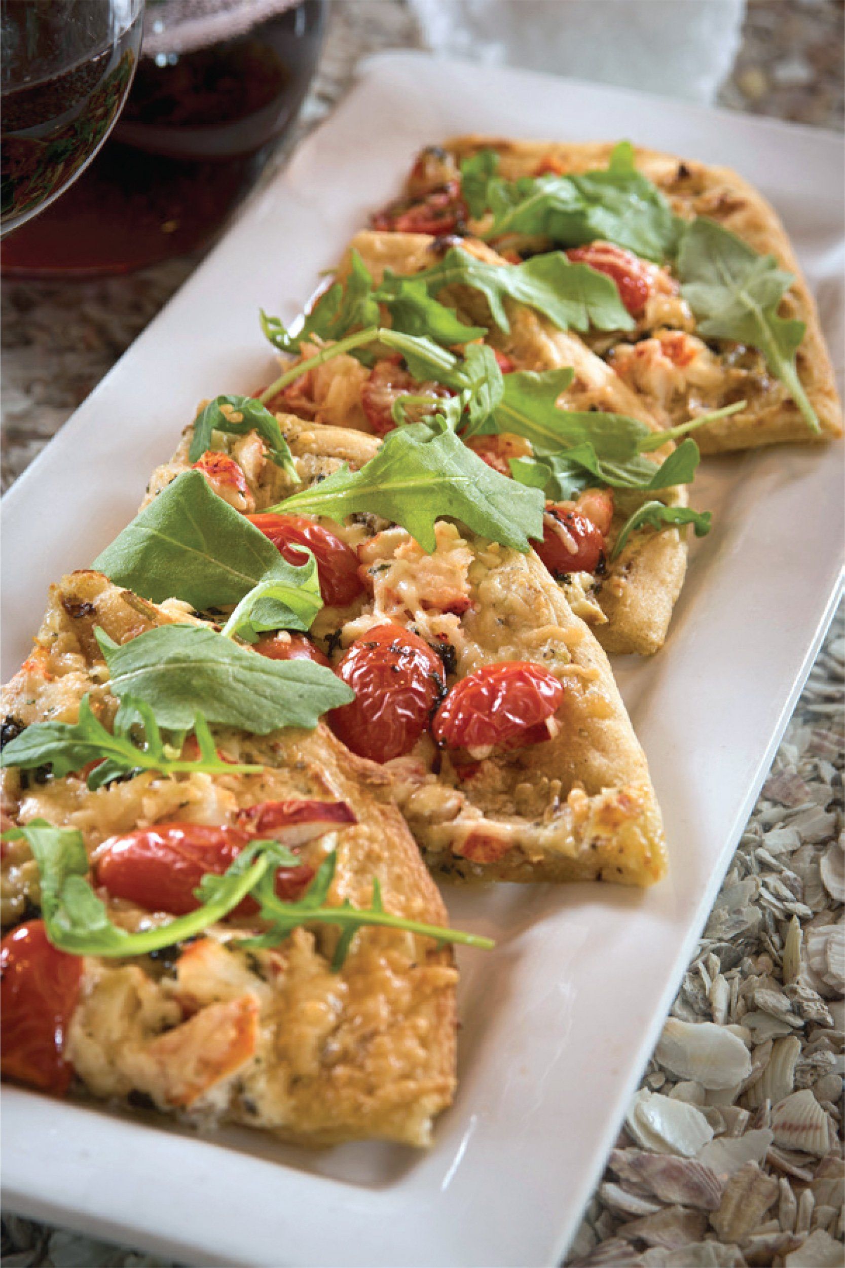 Flatbread slices with arugula, tomatoes, and cheese on a rectangular white plate.