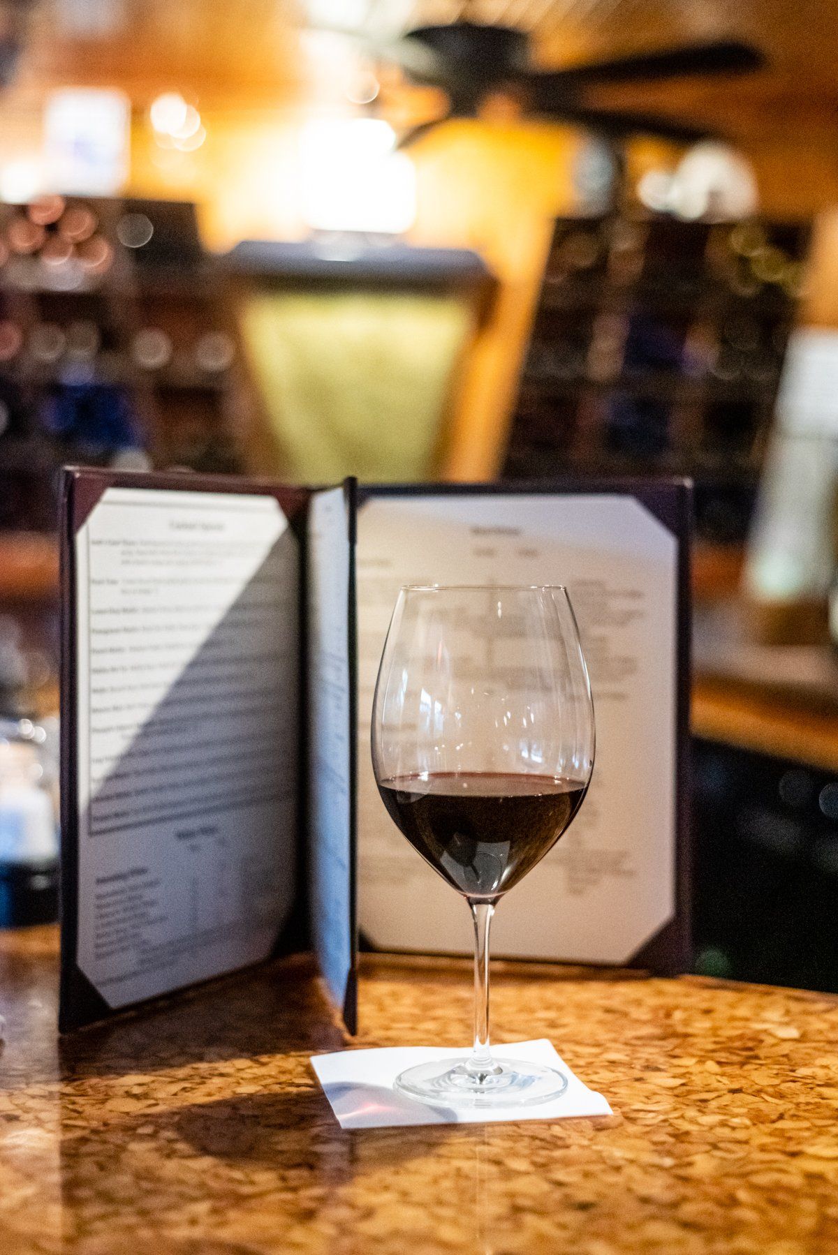 Wine glass filled with red wine on a bar, with menu in background.