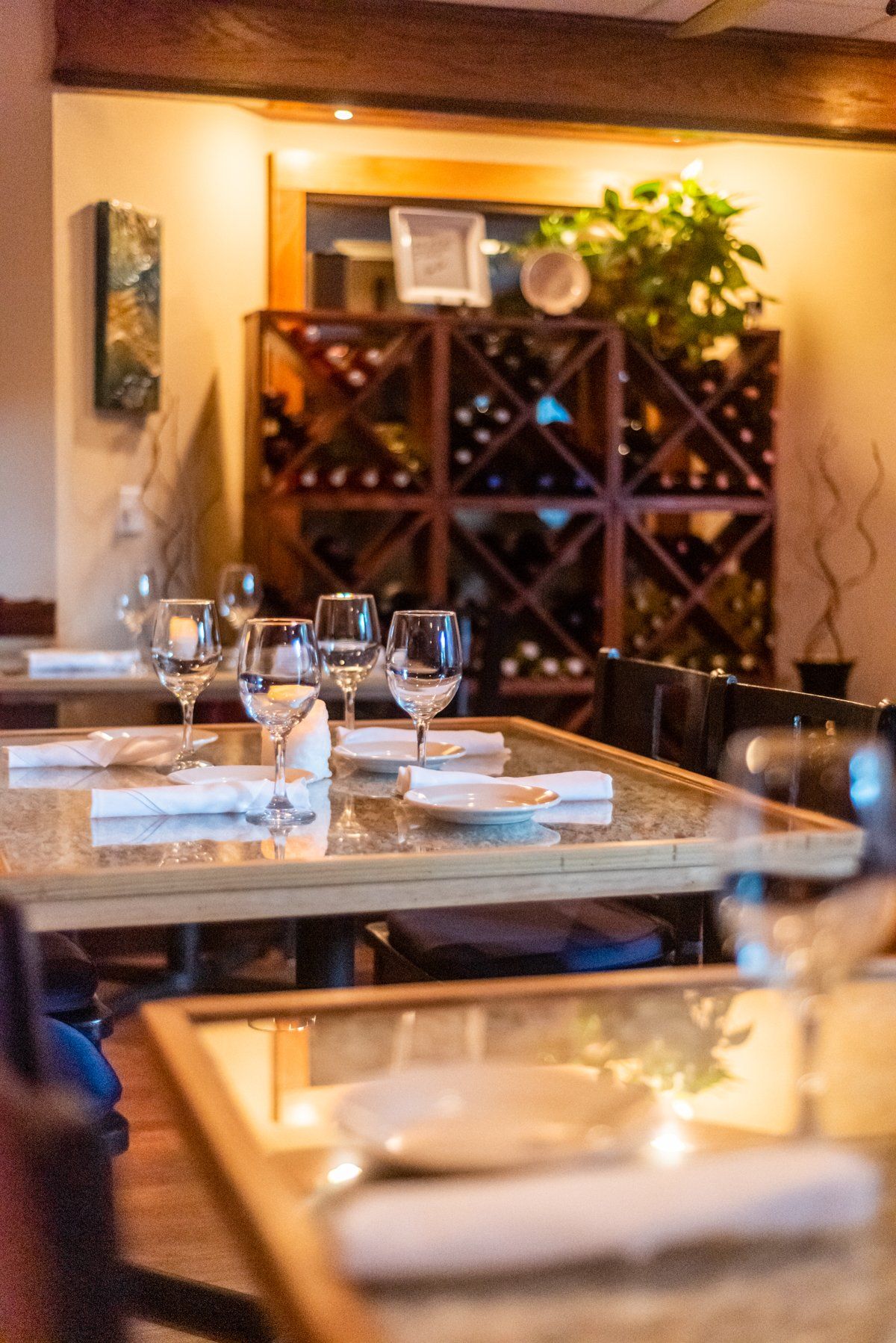 Restaurant dining room with tables set for service, wine rack, and warm lighting.