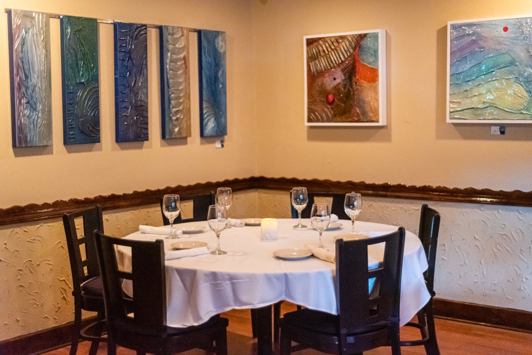 A round dining table set for six in a restaurant, with art on the walls.