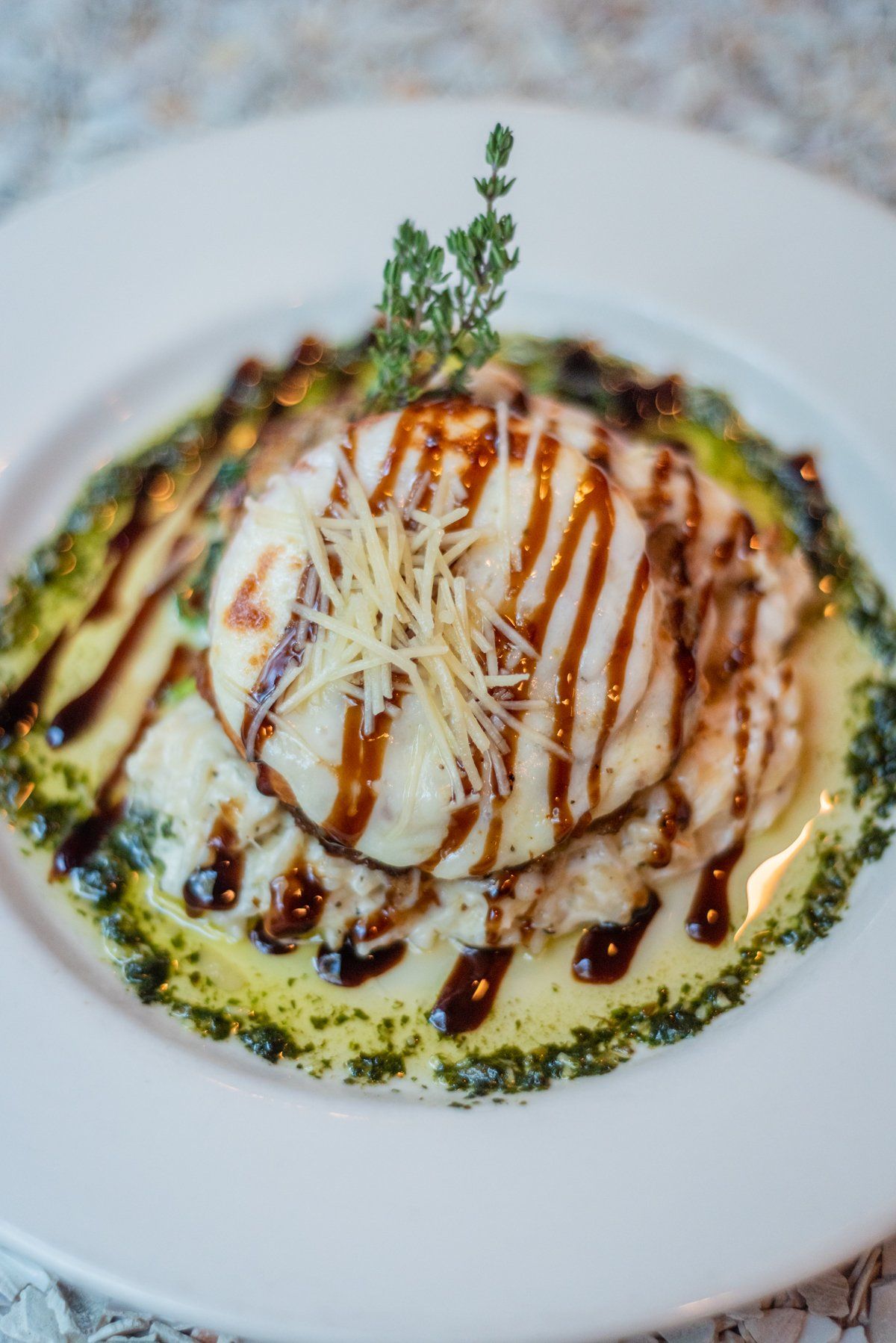 Dish with a fried or baked patty, creamy sauce, pesto, balsamic glaze, and garnish.