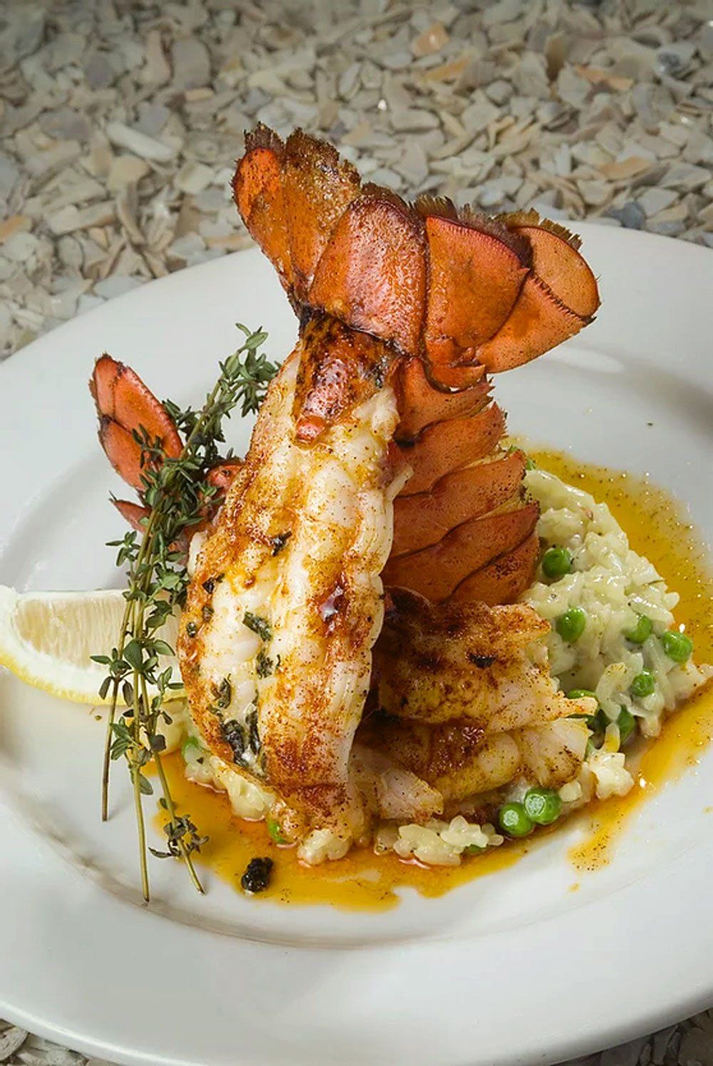 Grilled lobster tail on risotto with peas, garnished with thyme and lemon slice.