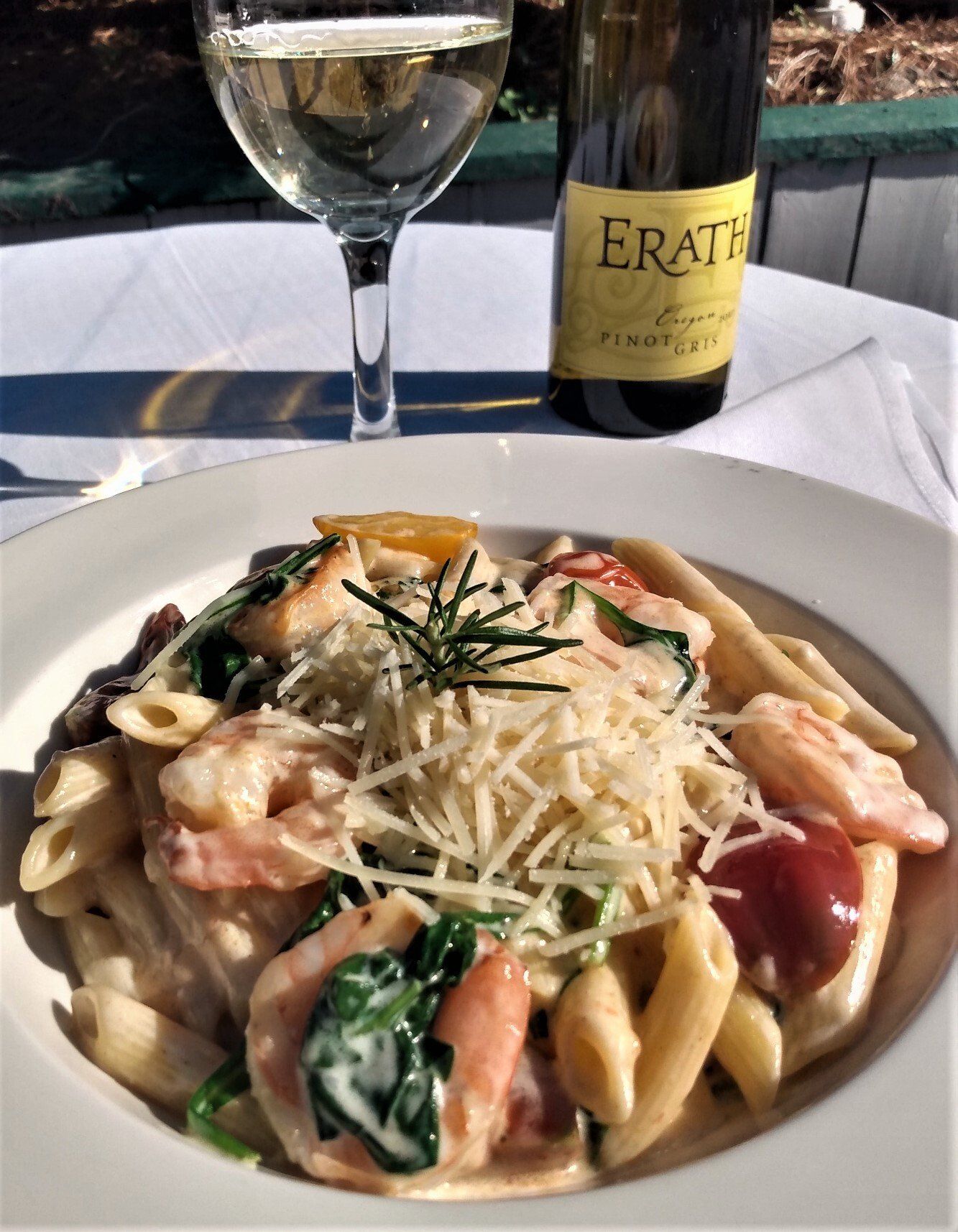 Pasta dish with shrimp, spinach, and grated cheese, paired with white wine and bottle on a white tablecloth.