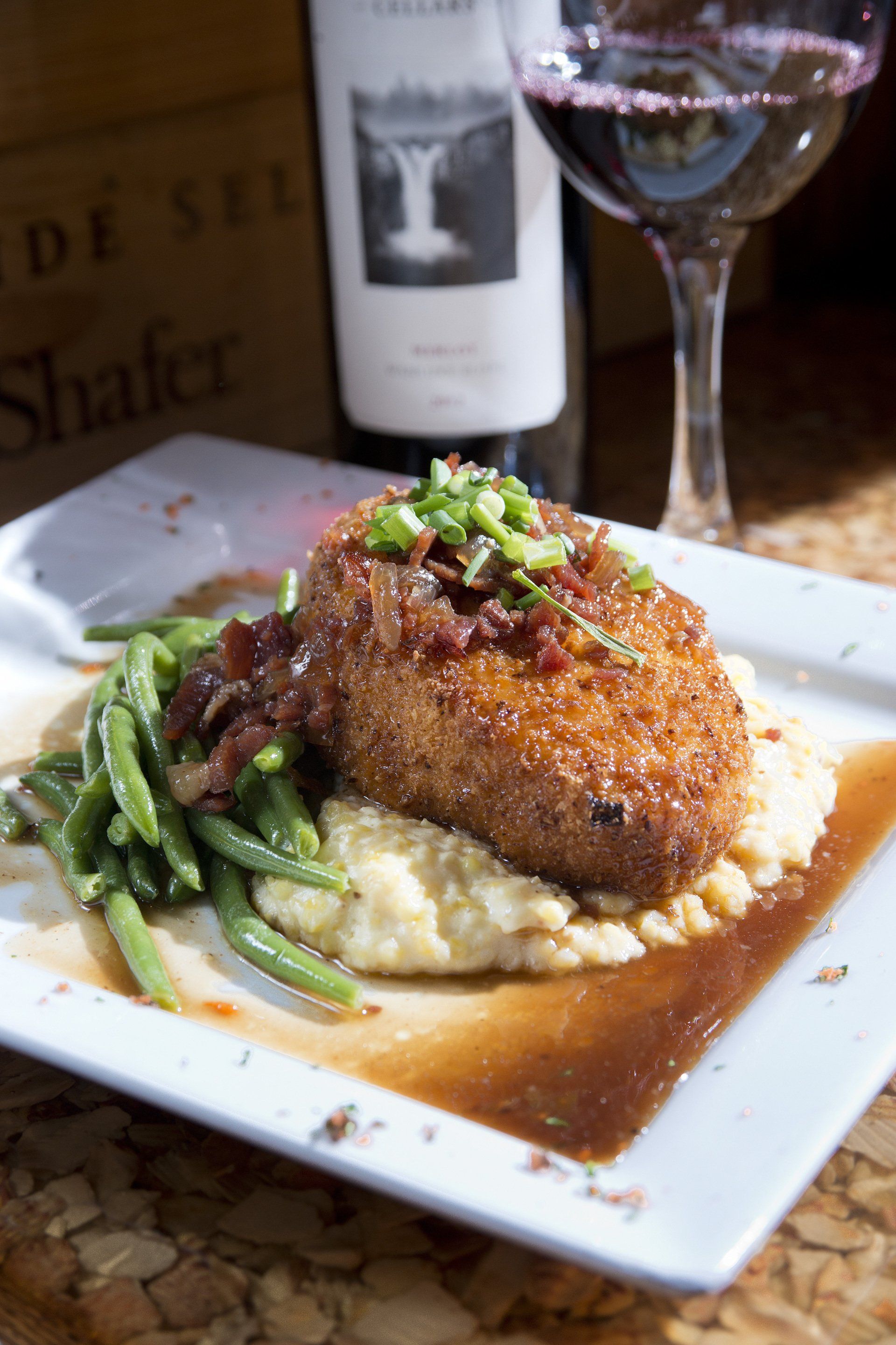 Plate with fried food, mashed potatoes, green beans, sauce, wine glass, wine bottle.
