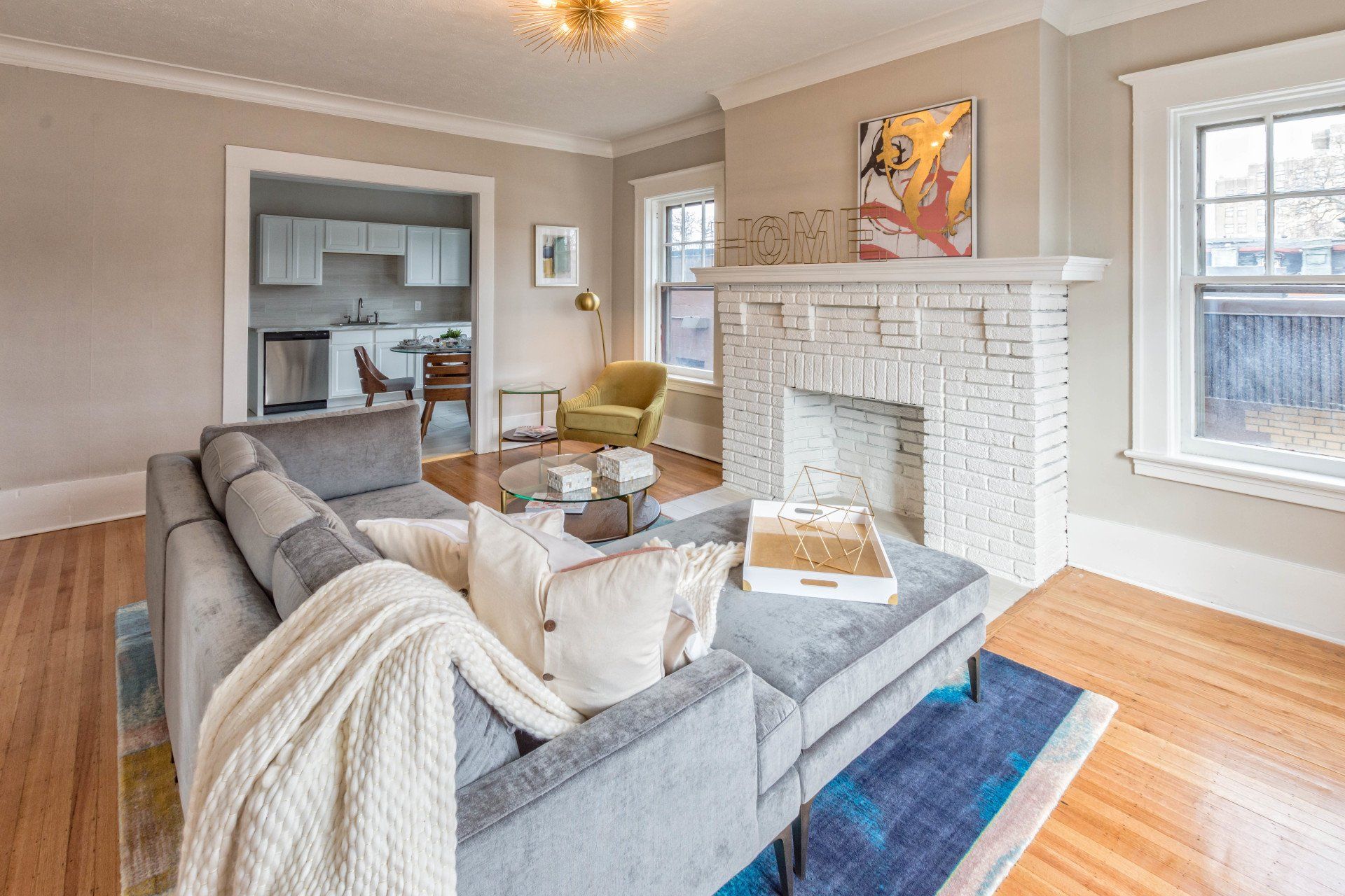 Living room off of kitchen with original fireplace, hardwood floors, and bright natural lighting
