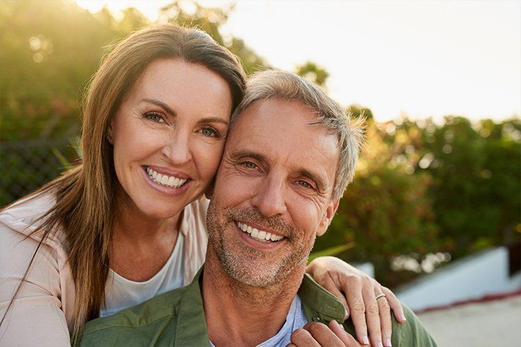 A woman is hugging a man from behind and they are smiling for the camera.