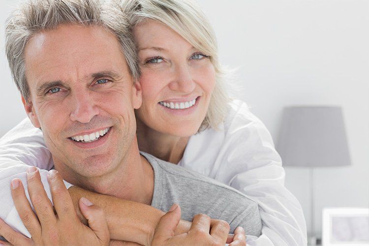 A man and a woman are hugging each other and smiling for the camera.