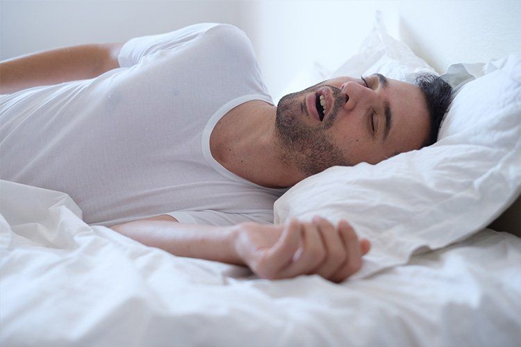 A man is sleeping on a bed with white sheets and pillows.