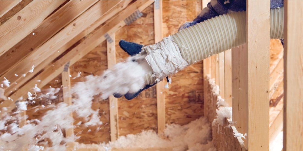 A person is blowing insulation into the attic of a house.