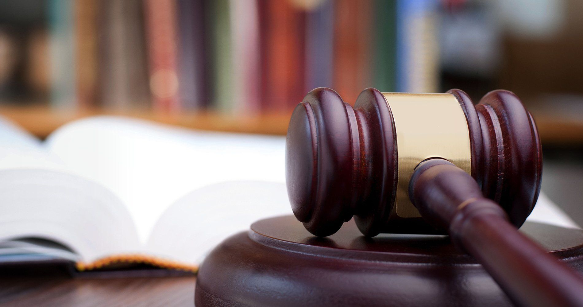 Judge’s gavel on a desk beside an open book, with blurred law books in the background.