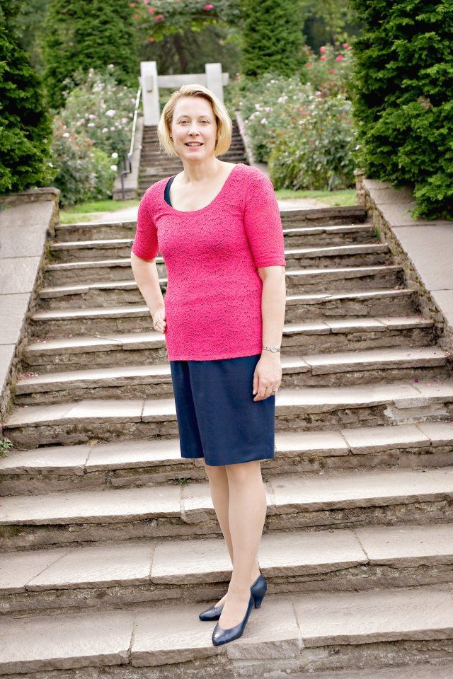 Woman in a pink top and blue skirt standing on stone steps in a garden.