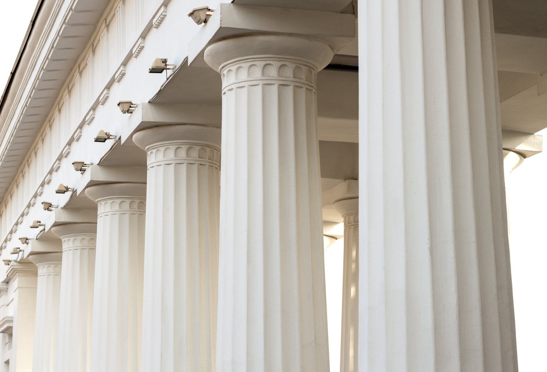 White classical columns lining a grand colonnade with ornate capitals and beams overhead