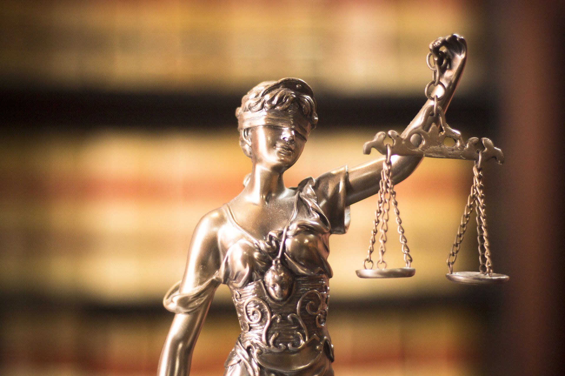 Silver Lady Justice statue holding scales, with blurred law books in the background