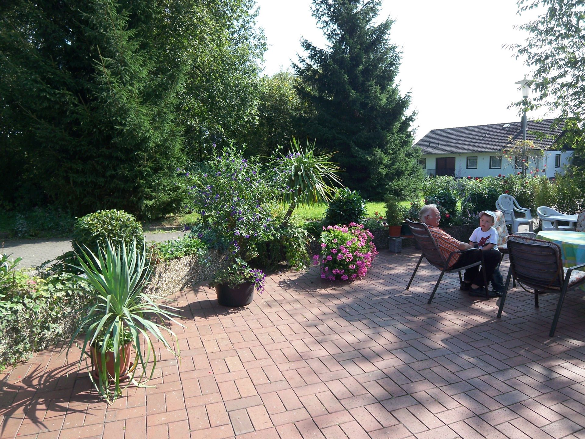 Ein Mann sitzt auf einem Stuhl auf einer Terrasse vor einem Haus