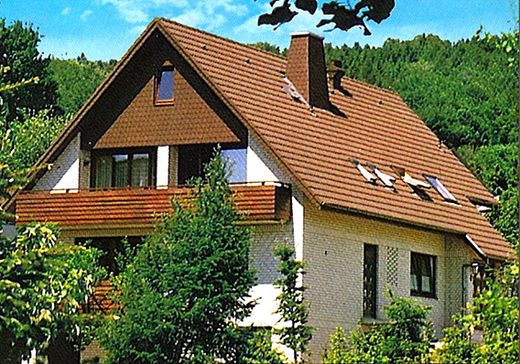 Ein weißes Haus mit einem braunen Dach ist von Bäumen umgeben