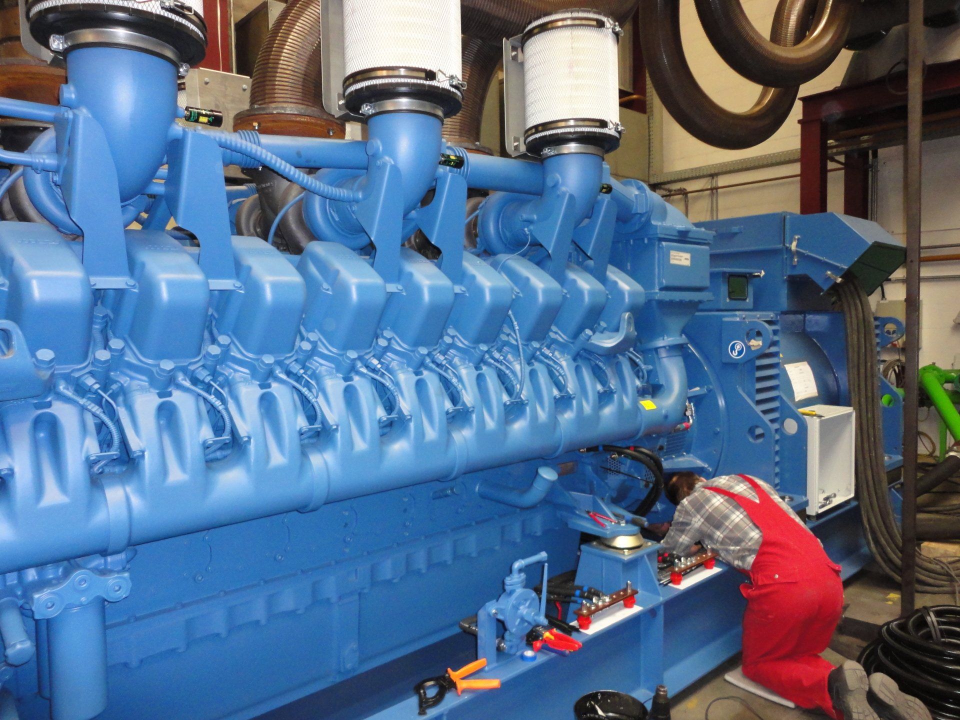 Un homme en salopette rouge travaille sur un moteur bleu
