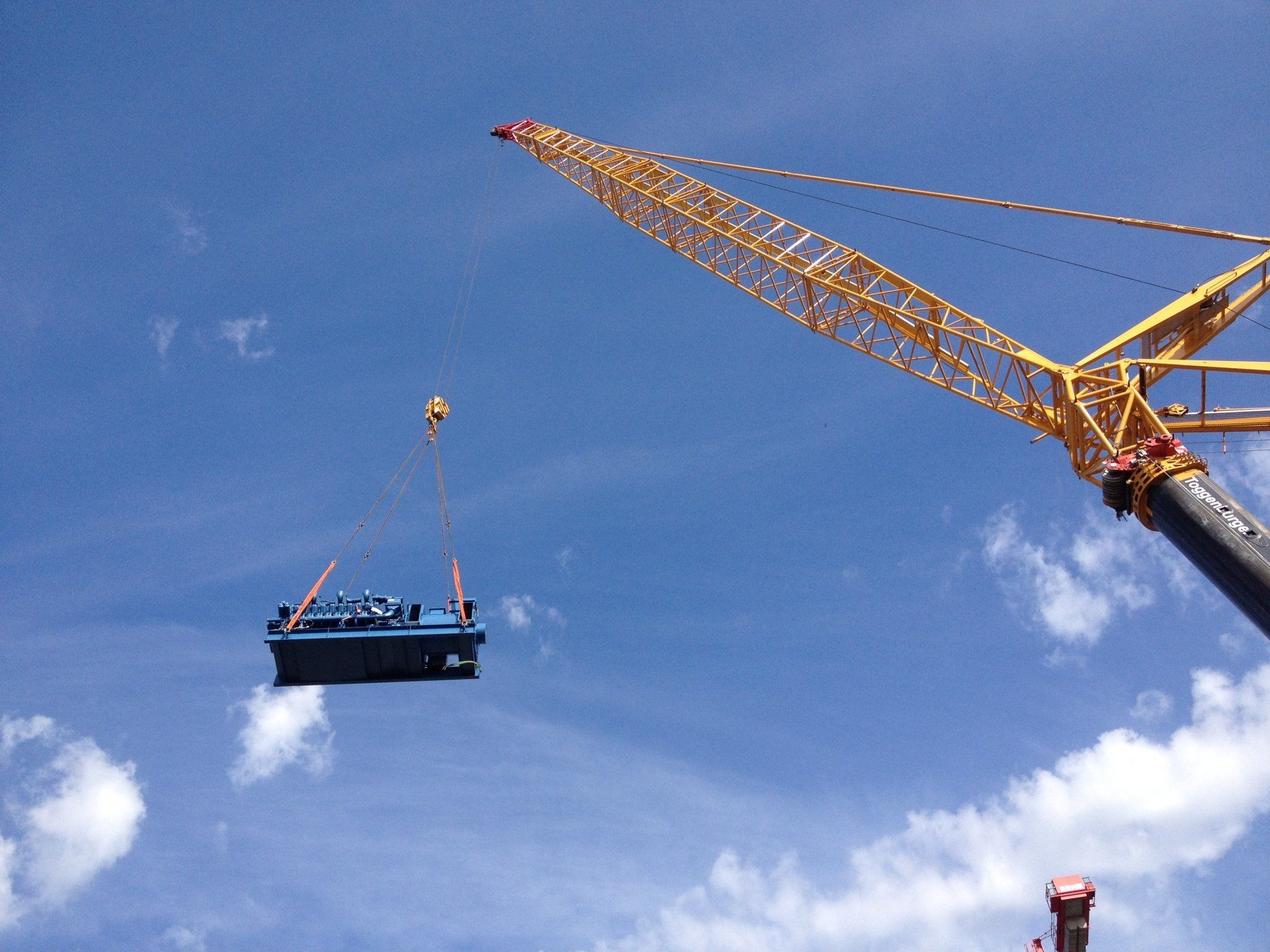 Une grande grue jaune soulève une boîte bleue dans les airs