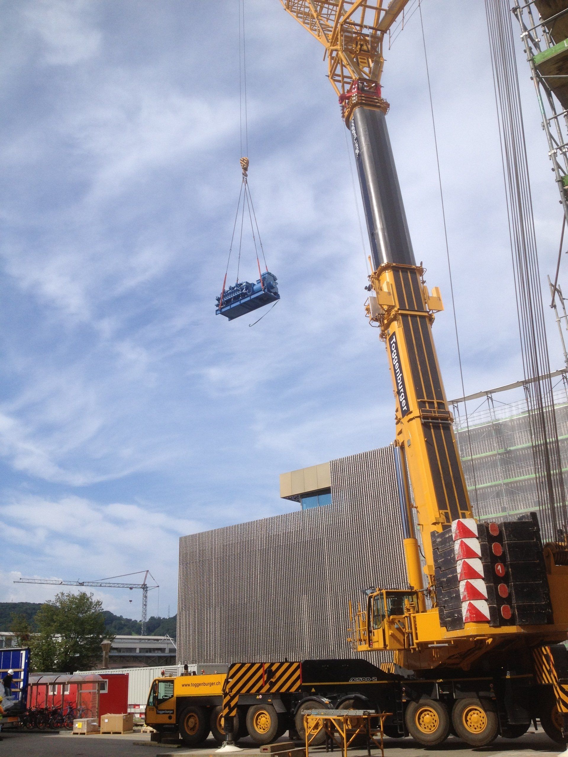 A large yellow crane is lifting a blue car