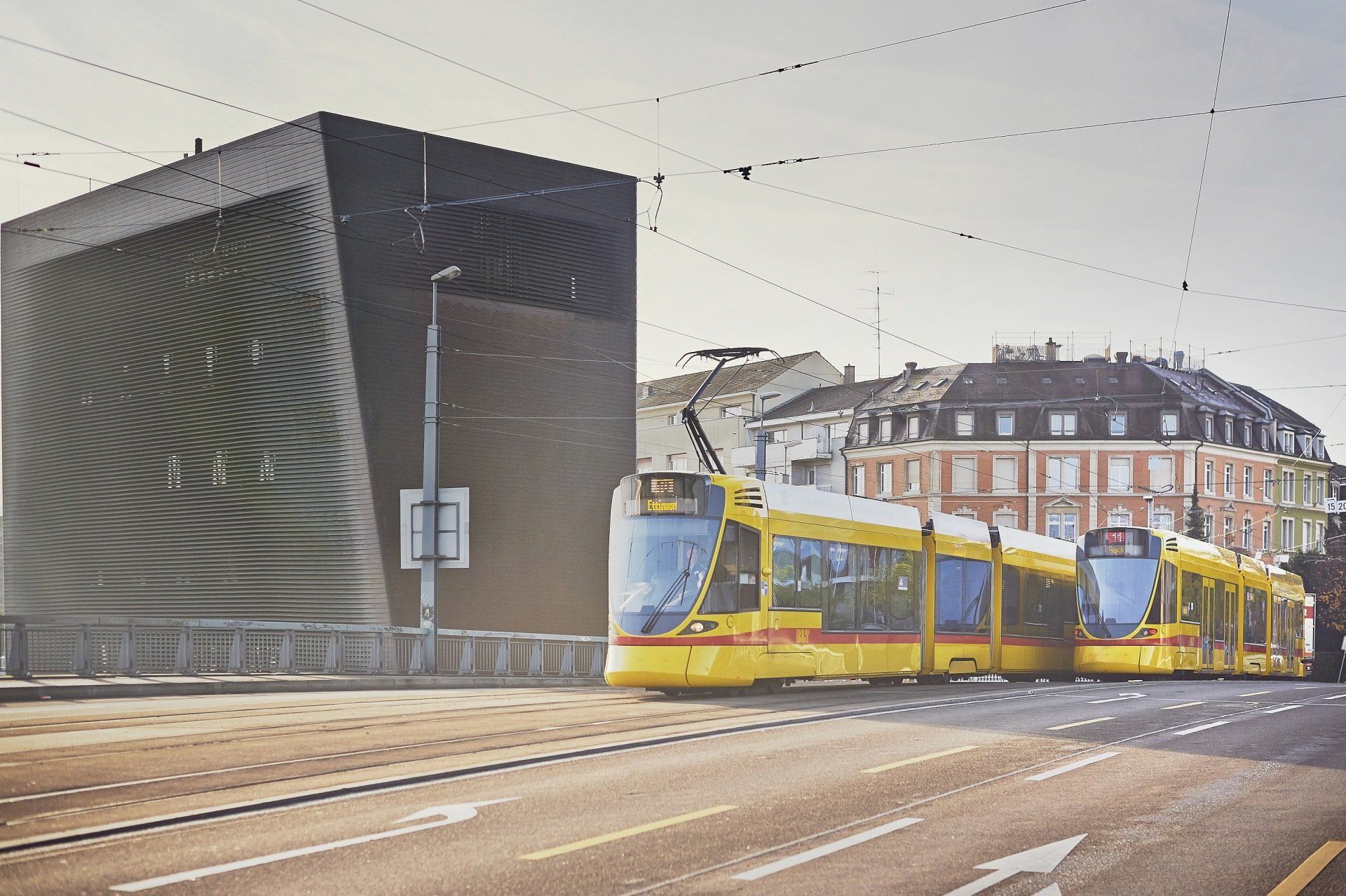 Ein gelber Zug fährt die Straße vor einem Gebäude entlang