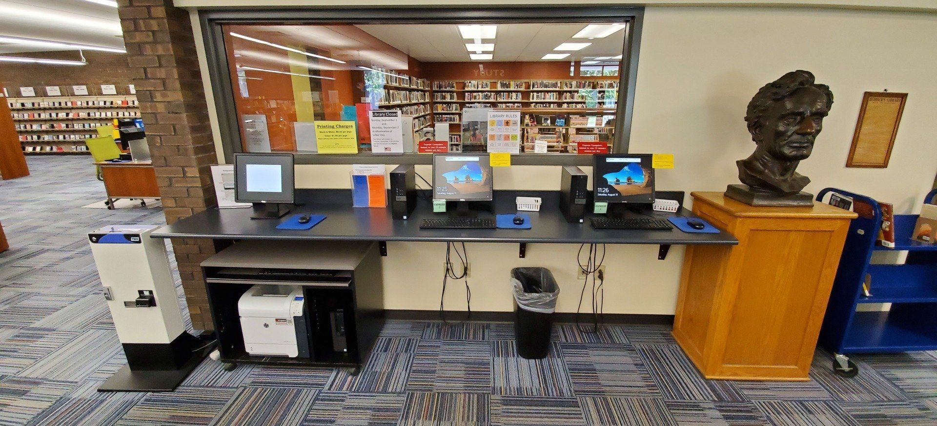 A computer desk in a library with a statue of abraham lincoln in the background.