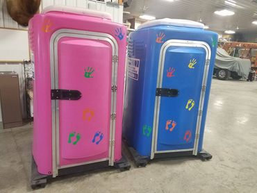 Two colorful porta-potties, one pink and one blue, decorated with handprints and footprints.