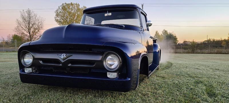 A blue pickup truck is parked in a grassy field.