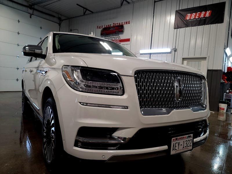 A white lincoln navigator is parked in a garage next to a sign that says break.