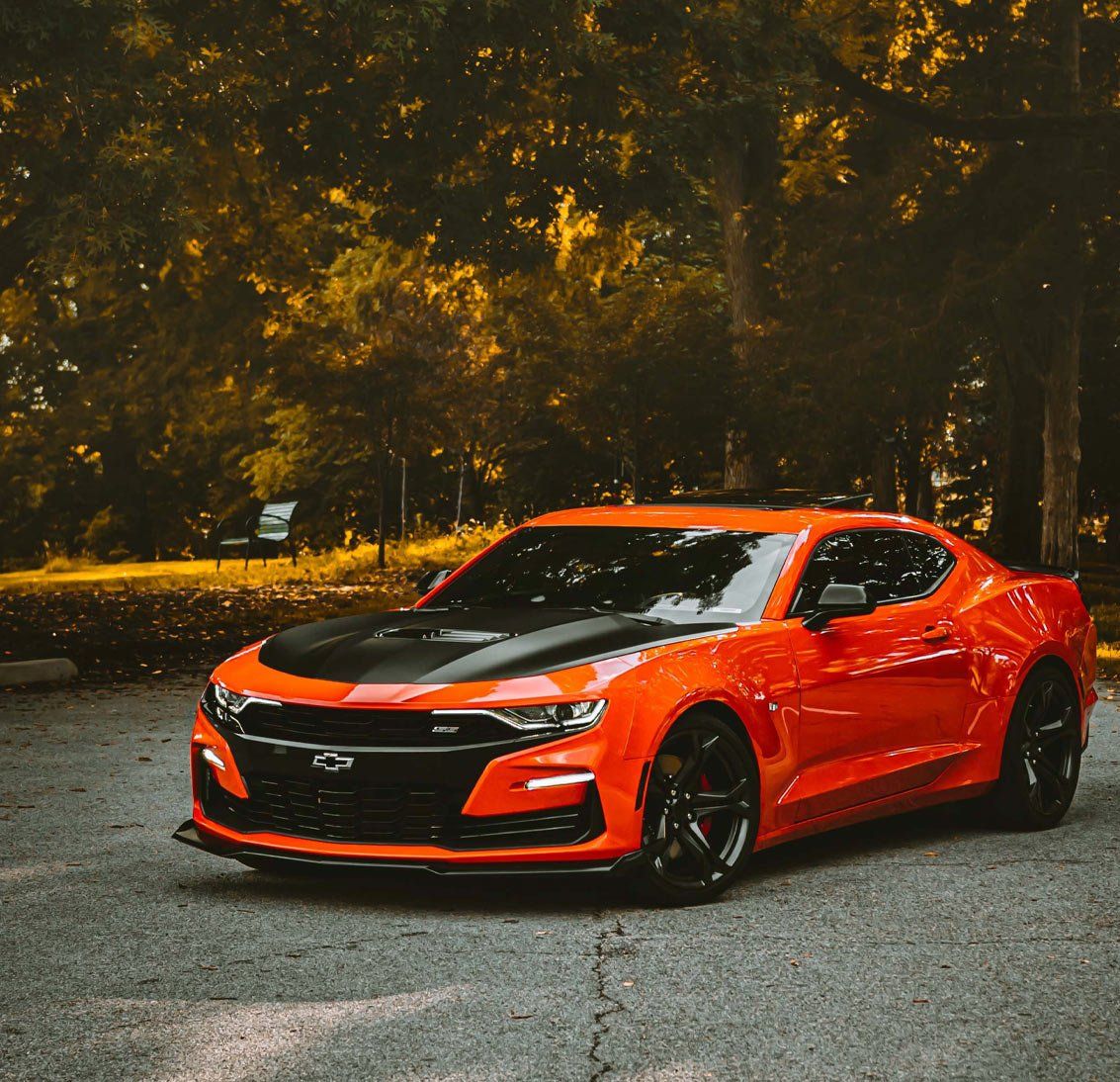 A red sports car with a black hood is parked in a parking lot.