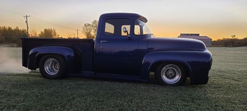 A blue pickup truck is parked in a grassy field at sunset.