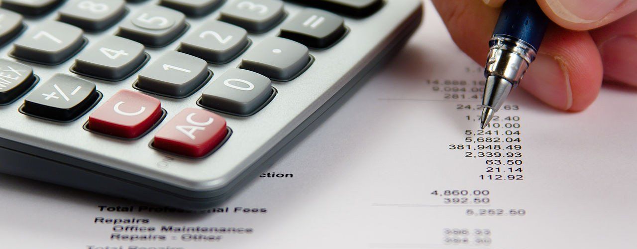 A person is writing on a piece of paper next to a calculator.