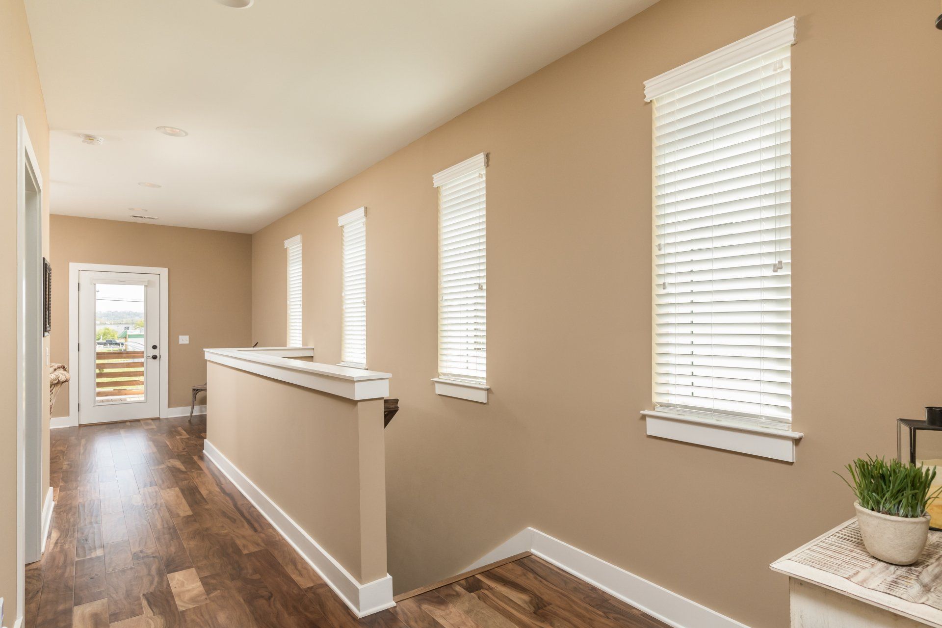 A hallway in a house with wooden floors and blinds on the windows.