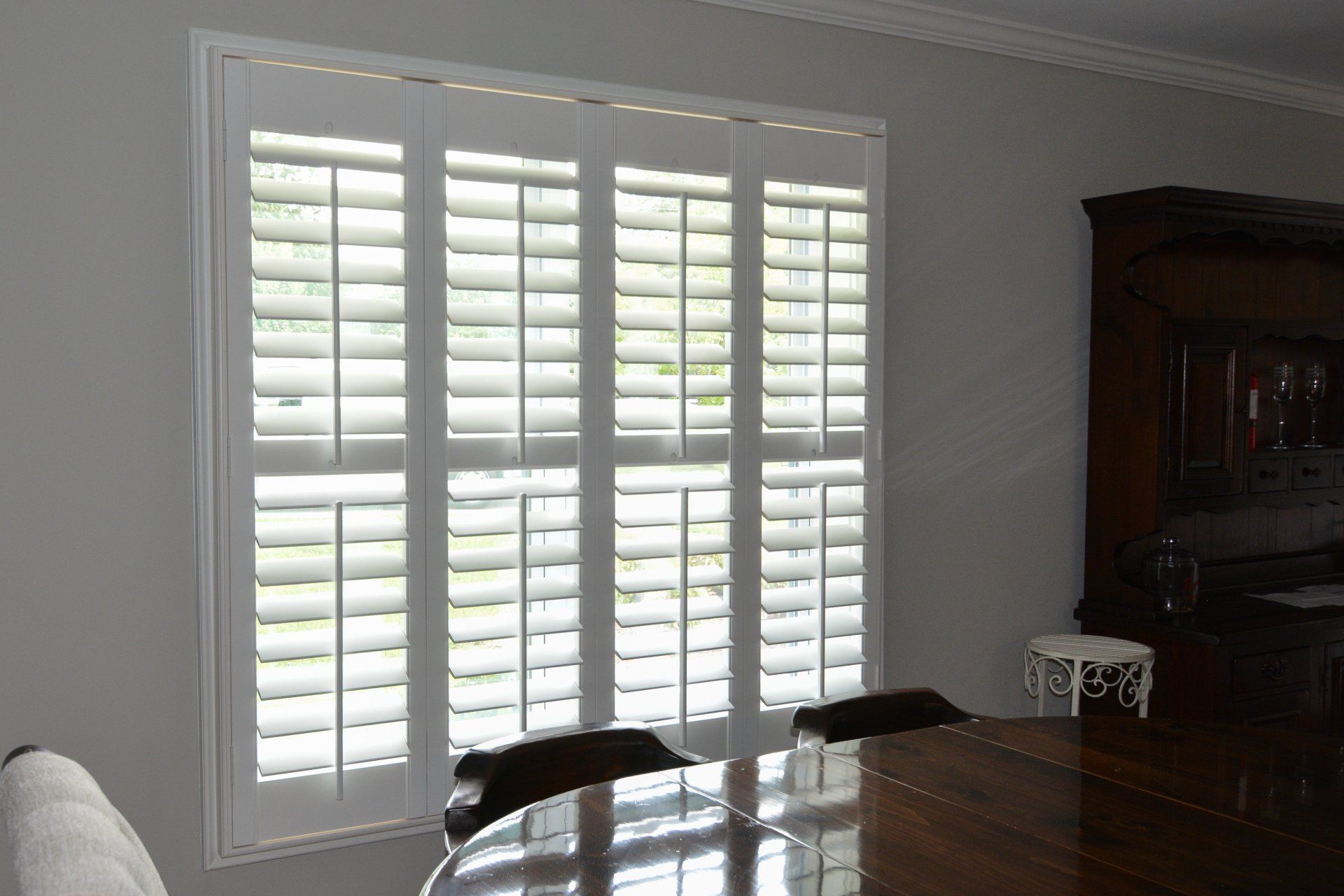A dining room with a table and chairs and white shutters on the windows.