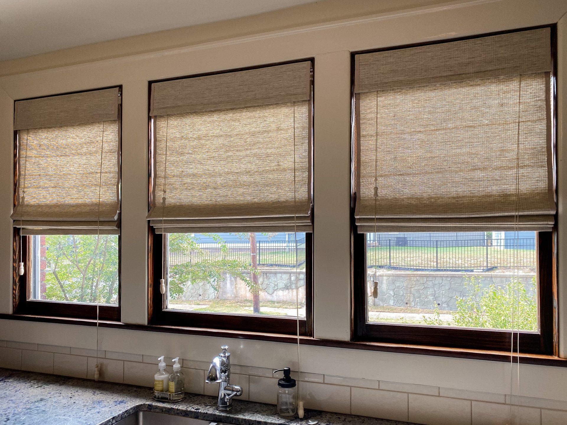 A kitchen with a sink and three windows with roman shades.